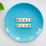 Innovative meal planning concept using alphabet tiles on a blue plate with green leaves.