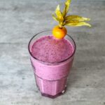 Delicious homemade purple smoothie in a glass topped with a vibrant physalis fruit.