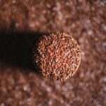 A top-down view of a jar filled with flax seeds, surrounded by scattered seeds on the surface.