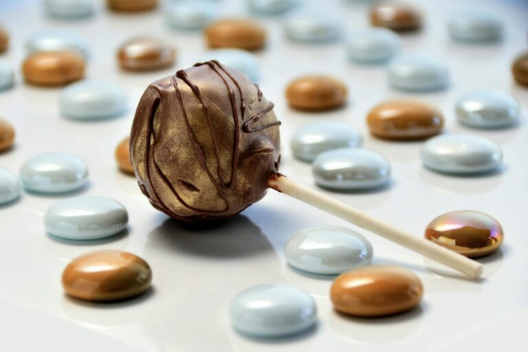 Decadent chocolate cake pop surrounded by colorful candy gems on a reflective surface.